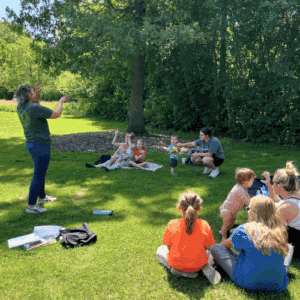 patrons sitting in the grass following along to a storytime in the park
