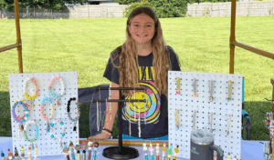 Girl Smiling behind craft table full of beaded jewelry at artisan faire