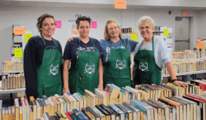friends of the library members posing and smiling behind stacks of books
